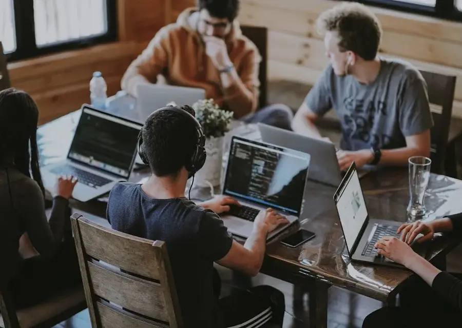 Një ekip që bashkëpunon në laptopë rreth një tavoline pune të përbashkët