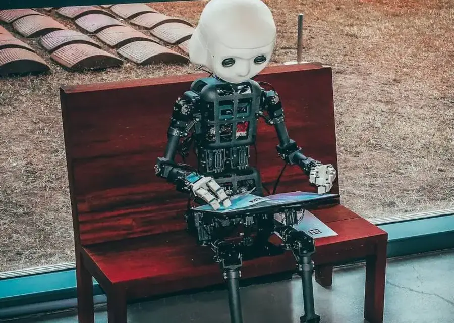 Një robot humanoid duke lexuar nga një tablet, ilustron automatizimin IT që heq punën manuale të përsëritur